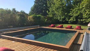 A rectangular swimming pool with a wooden deck and red cushions. - Large house with plenty of charm (Aureilhan)