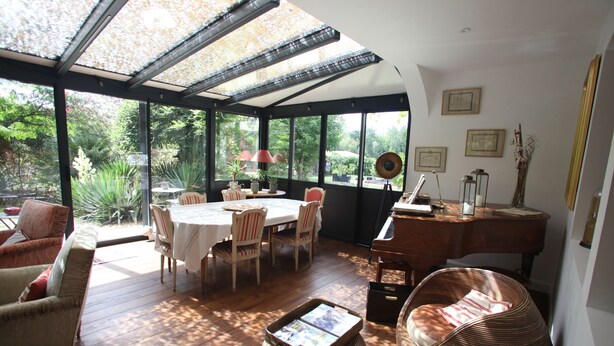A sunlit room with a glass ceiling, wooden flooring, a round table, and wicker furniture. - Large house with plenty of charm (Aureilhan)