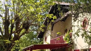 A two-story house with a balcony, surrounded by lush greenery and vibrant flowers. - Large house with plenty of charm (Aureilhan)