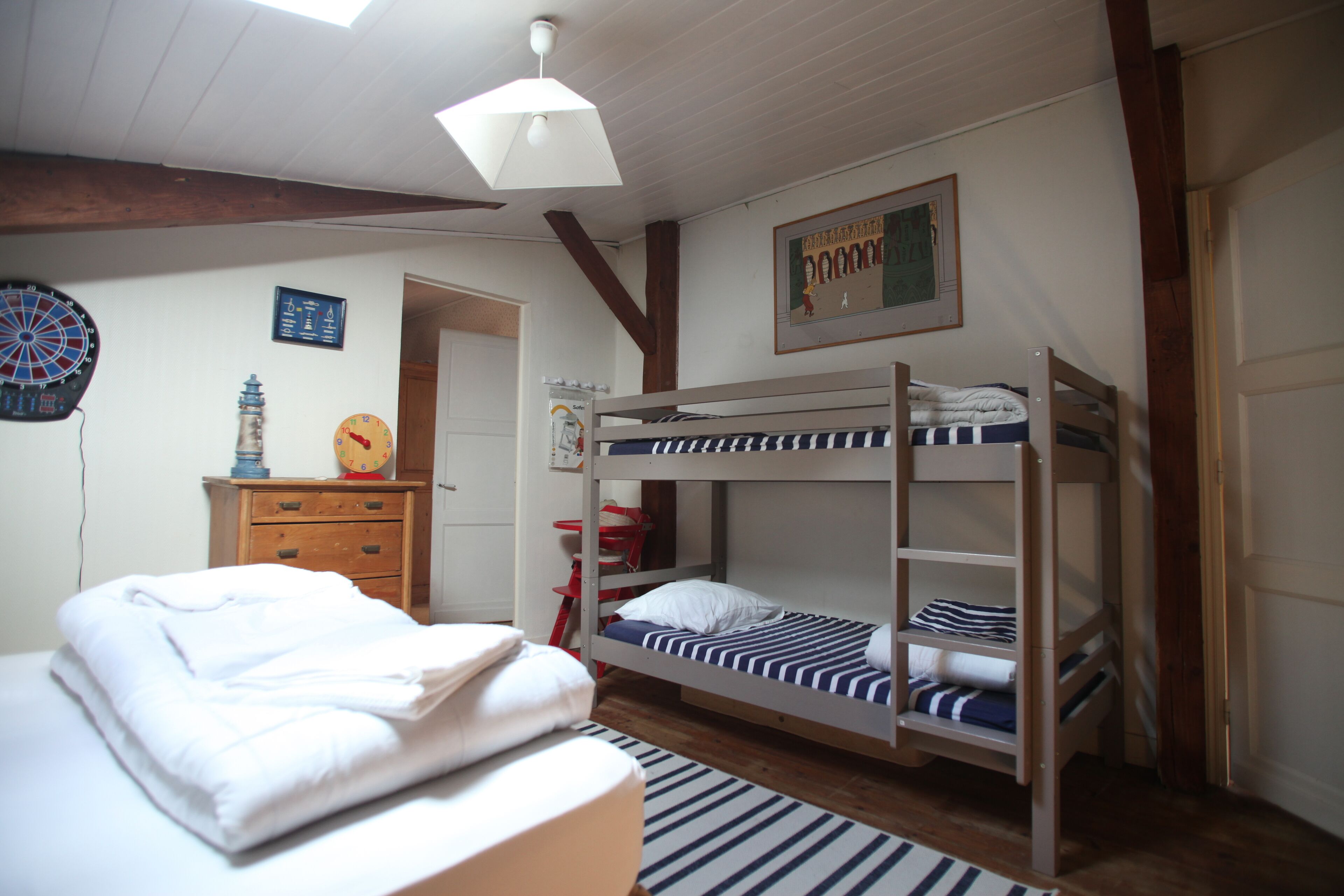 A bunk bed room with a wooden ceiling, a white bed, a red chair, and a dartboard on the wall.