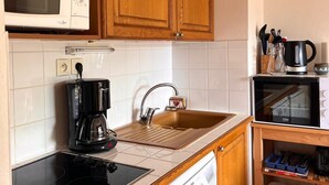 Eine kompakte Küche mit Holzausstattung, einer Mikrowelle, einer Kaffeemaschine, einem Spülbecken und einem Geschirrspüler.