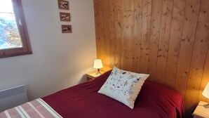 Ein Schlafzimmer mit einem hölzernen Kopfteil, einem Bett mit roter Decke, einer Nachttischlampe und einem Fenster mit Blick auf Bäume.