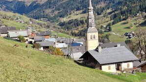 Ein ländliches Dorf mit einem markanten Kirchturm, umgeben von Häusern und einer Bergkulisse.