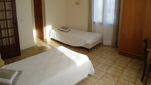 Una habitación con dos camas individuales, un armario de madera y una puerta con panel de vidrio satinado.