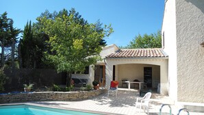 Una piscina con muro de piedra y un patio cubierto con mobiliario exterior.