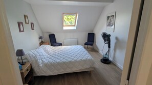 A bedroom with a bed, two chairs, a standing fan, a window, and a radiator. - Charming country house near Saint-Valery-Sur-Somme, 6 people (Arrest)