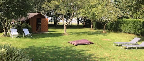 A grassy outdoor area with a wooden shed, two lounge chairs, and a purple cushion.