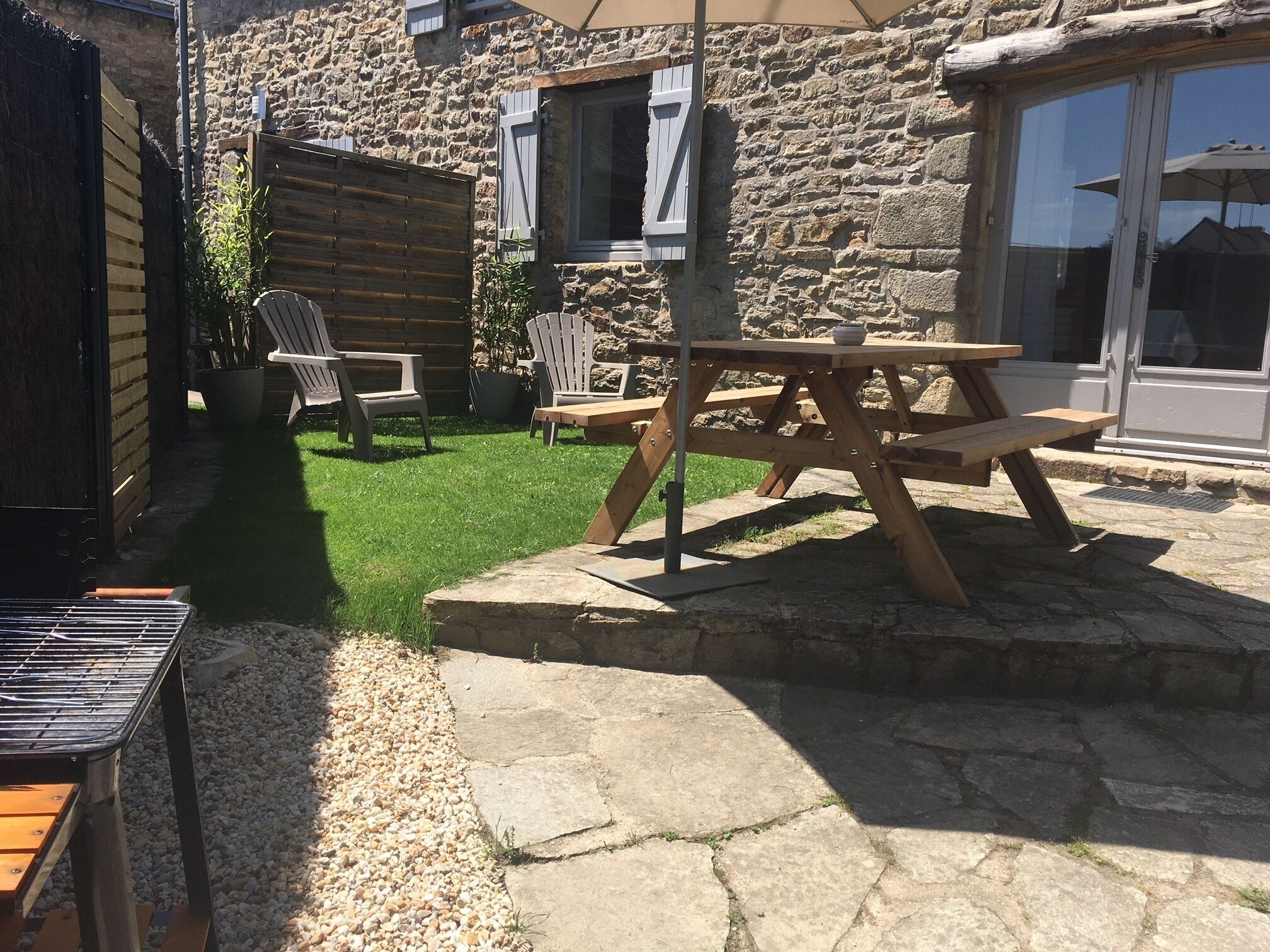 Un bâtiment en pierre doté d’une terrasse en bois, d’une table de pique-nique et de sièges d’extérieur.