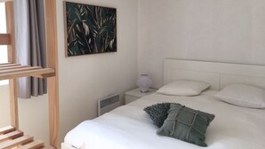 Ett sovrum med en säng, ett nattduksbord, ett element, ett fönster med gardiner och ett konstverk som hänger på väggen.