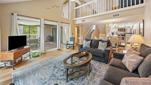 A spacious living room with a large flat-screen TV, a comfortable sofa, and a dining area with a chandelier.