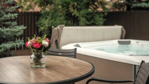 A round wooden table with a vase of flowers, a hot tub, and a wooden fence in the background. - Sunshine Retreat-Hot Tub,Massage Chair,Espresso&EV (Bend)