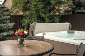 Una mesa redonda de madera con un florero, un jacuzzi y una valla de madera al fondo.