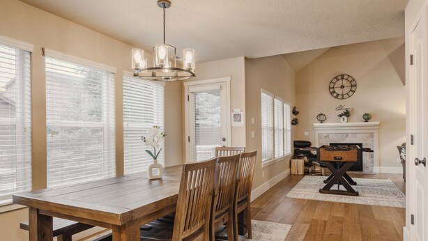 A dining area with a wooden table and chairs, a chandelier, and a fireplace with a clock above it. - Sunshine Retreat-Hot Tub,Massage Chair,Espresso&EV (Bend)