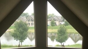 Una habitación con vistas a un lago y casas a través de dos ventanas.