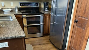 Una cocina con nevera de acero inoxidable, dos hornos, cafetera y encimera de granito.