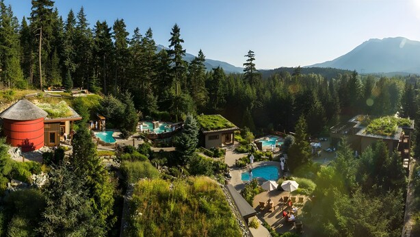 Un complejo turístico con varias piscinas, un alto depósito de agua y montañas al fondo.