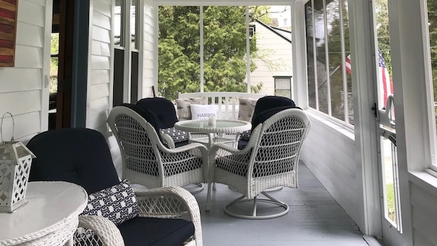 A covered porch with wicker furniture and a table, overlooking a green landscape. - Harbor House located in the heart of Ephraim! (Ephraim)