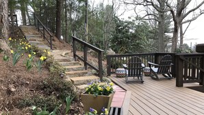 Une terrasse en bois avec un escalier en pierre menant à l’étage supérieur, entourée de plantes en pot et de mobilier d’extérieur.
