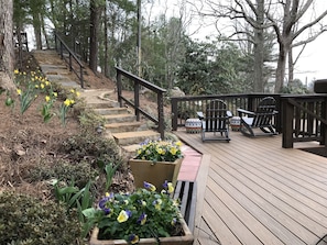 Una terraza de madera con una escalera de piedra que sube, rodeada de macetas con plantas y mobiliario de exterior.