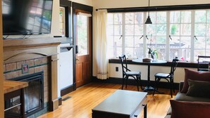 Un vaste espace de vie doté d’un téléviseur à écran plat, d’un ventilateur de plafond, d’une cheminée, d’une table à manger avec des chaises et de grandes fenêtres offrant une vue sur l’extérieur.