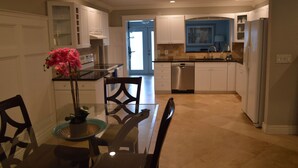 A modern kitchen with white cabinets, a dishwasher, and a dining area with a glass table and chairs. - Temporary living that feels like home where you can relax and be yourself. (Maitland)