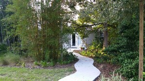 A garden pathway leading to a house with a white exterior and a door. - Temporary living that feels like home where you can relax and be yourself. (Maitland)