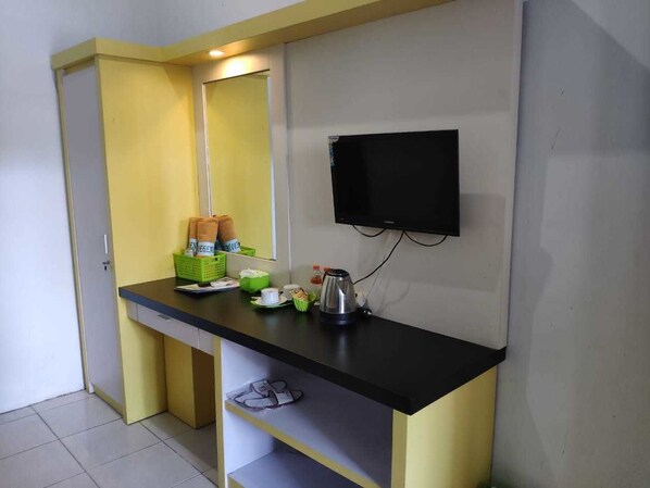 A compact kitchenette with a black countertop, a small sink, and a mirror. There is a flat-screen TV mounted on the wall above the counter.