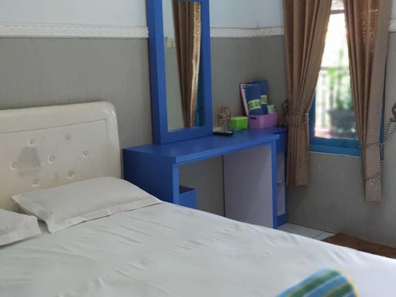 Un dormitorio con cama, un escritorio azul, un espejo y una ventana con cortinas.