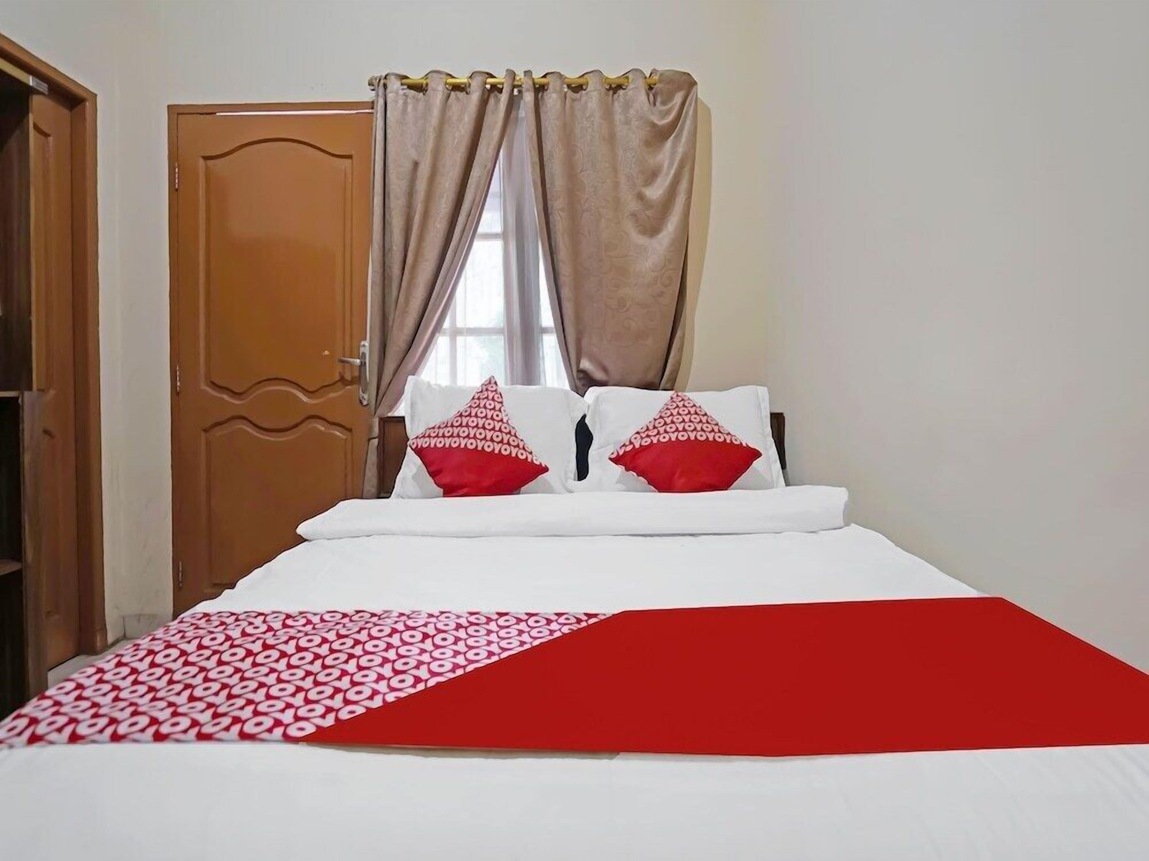 A bedroom with a bed, two pillows, a red and white blanket, and beige curtains.