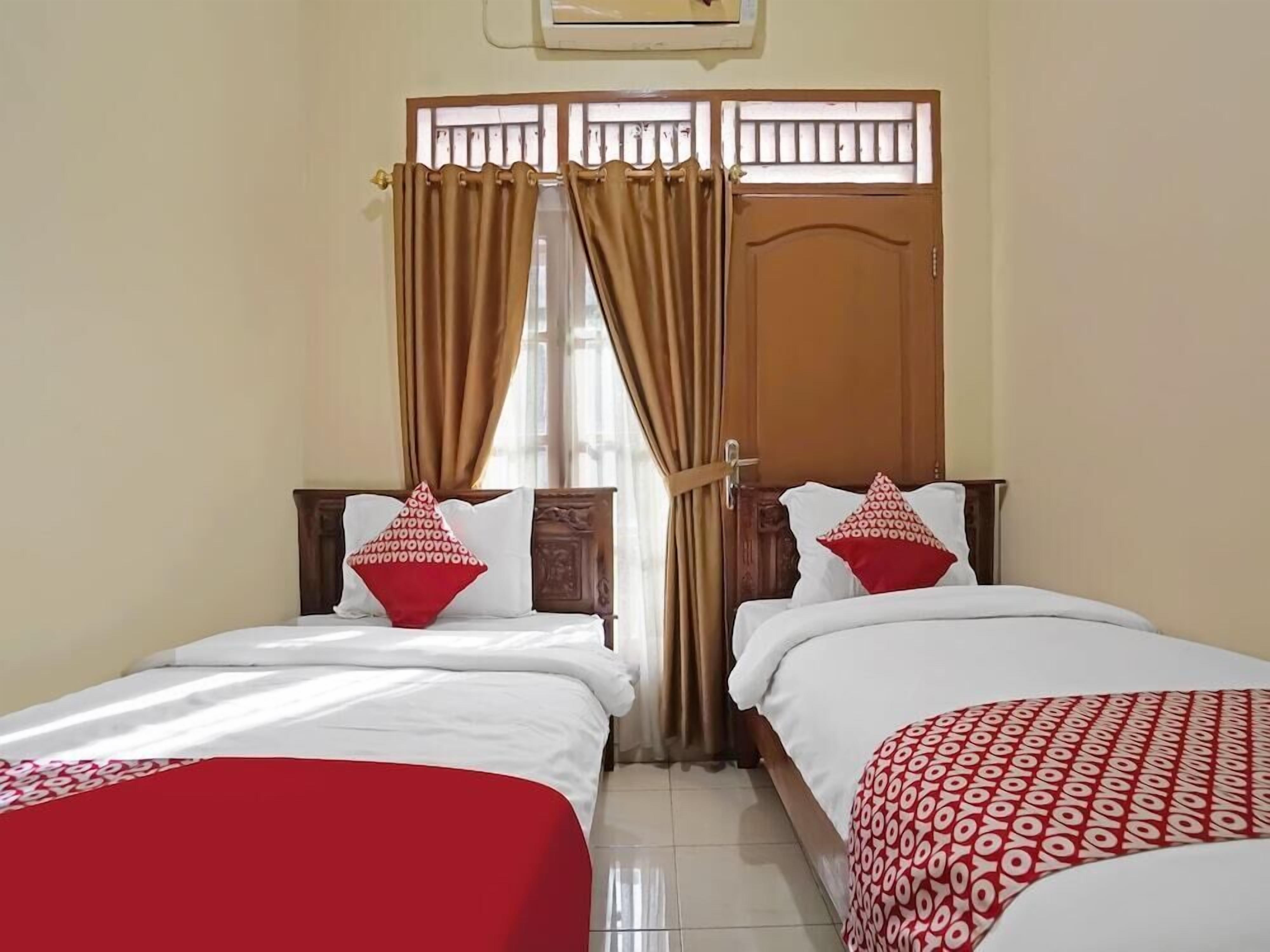 A hotel room with two single beds, a wooden door, a window with curtains, and a ceiling fan.
