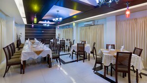 Un espace repas comprenant plusieurs tables et chaises, des luminaires au plafond et un lustre moderne.