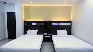 Habitación de hotel con dos camas individuales, cabecera oscura, mesita de noche pequeña con teléfono y televisor, y ventilador de techo.