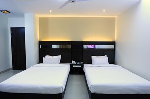 Habitación de hotel con dos camas individuales, cabecera oscura, mesita de noche pequeña con teléfono y televisor, y ventilador de techo.
