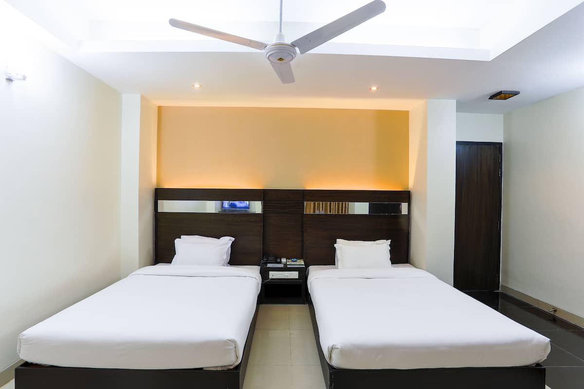A hotel room with two single beds, a ceiling fan, a nightstand with a phone and a remote control, and a large window with a view of the sky.