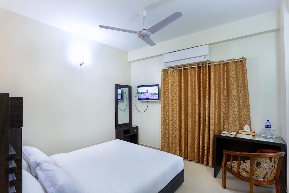 A hotel room with a bed, a desk with a chair, a television, and a ceiling fan.