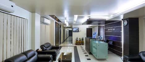 Un hall d’hôtel moderne avec un comptoir d’accueil, des canapés en cuir noir, une table basse en verre et un grand miroir.