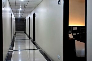 Un largo y estrecho pasillo de hotel con piso de baldosas brillantes, puertas a ambos lados y una lámpara empotrada en la pared derecha.