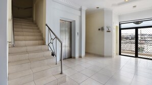 A spacious hallway with a staircase leading to an elevator. The walls are white, and there is a large glass door at the end of the hallway. - Collection O Mangga Besar Near Lokasari Square Formerly 45 Residence (Jakarta)