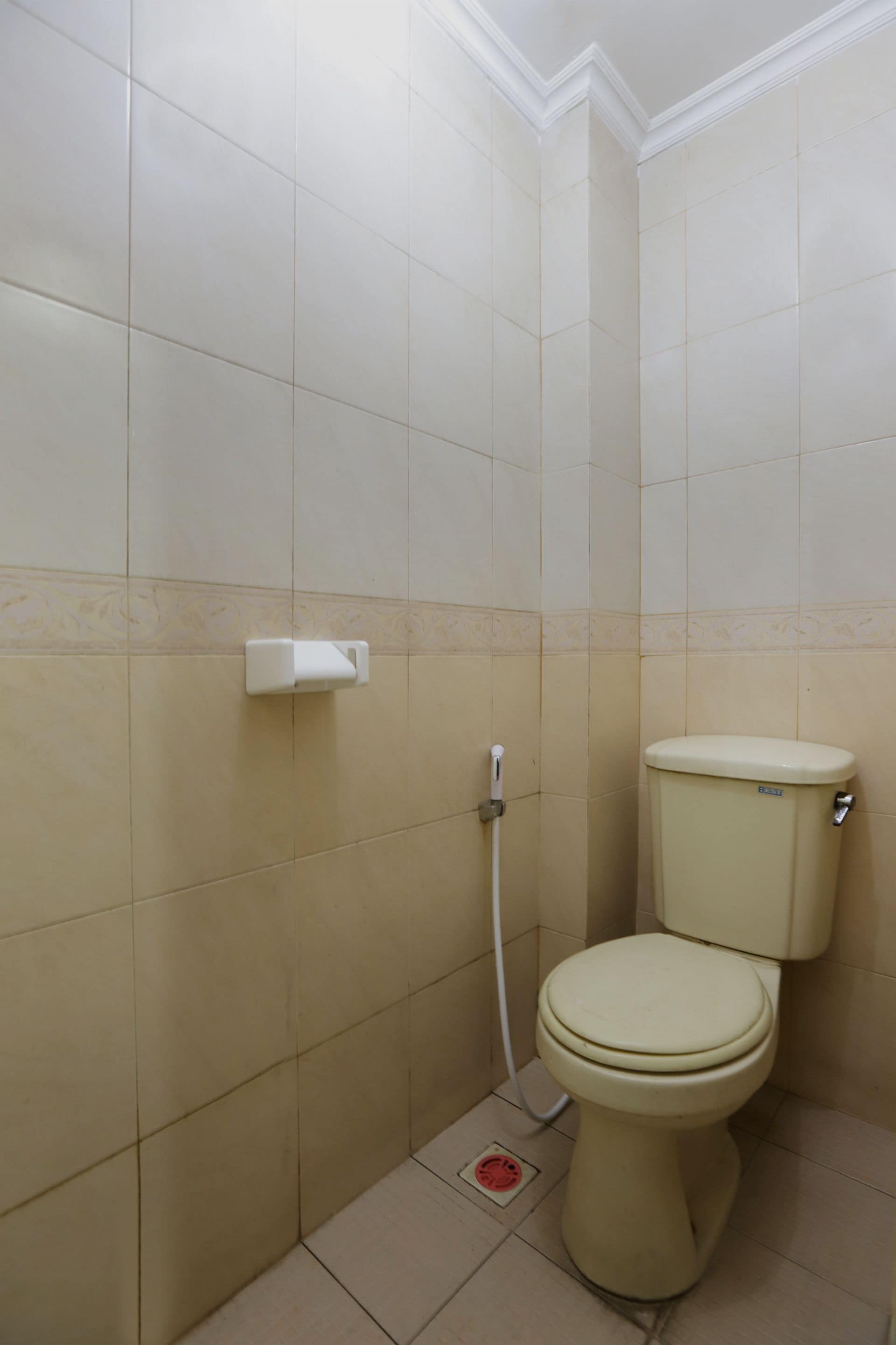Un baño pequeño con azulejos, un inodoro, un secador de manos y un desagüe en el suelo.