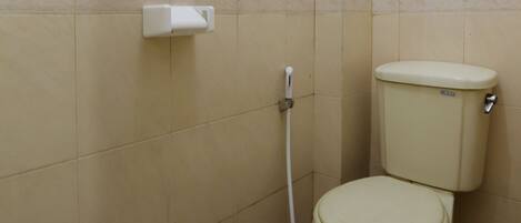 Un baño pequeño con azulejos, un inodoro, un secador de manos y un desagüe en el suelo.