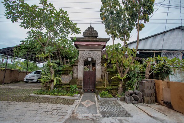 A traditional gate with intricate carvings, surrounded by lush greenery and a paved pathway leading to a building. - Ubud Paras Villa (Ubud)