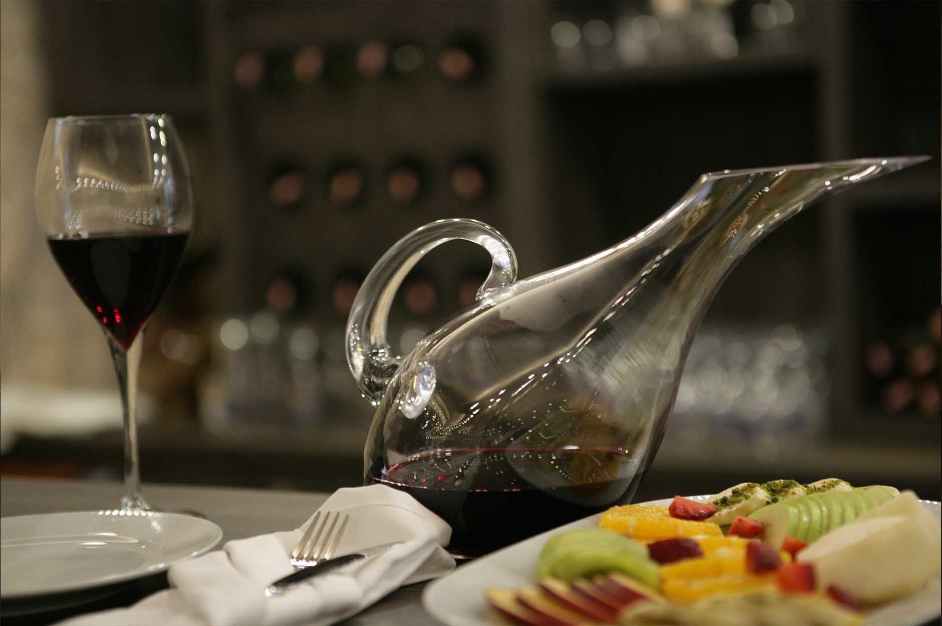 Una mesa con un jarro, una copa de vino tinto y un plato de comida.