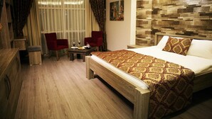 Une chambre d’hôtel avec un plancher en bois, un lit recouvert d’une couvre-lit à motifs, deux chaises rouges, une petite table avec un verre à vin et un tableau accroché au mur.