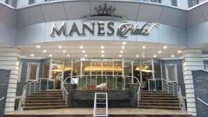 L’extérieur de l’hôtel Manes se distingue par une enseigne bien visible, une façade en verre et un escalier menant à l’entrée.