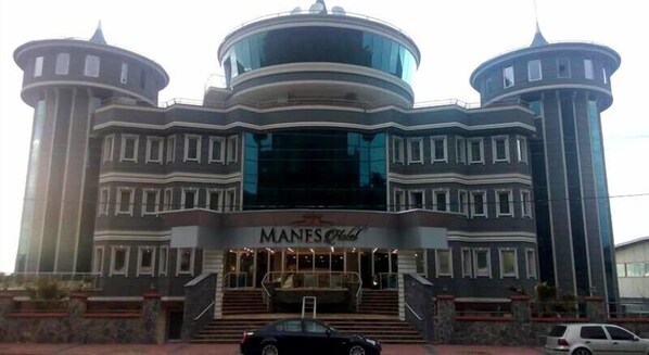 A building with a central glass facade, two cylindrical towers, and a sign reading "MANES OLD".