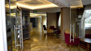 Un hall d’hôtel au design moderne, comprenant une cloison en verre, un comptoir d’accueil et des espaces de détente.