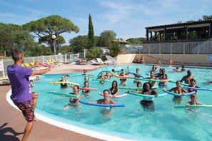 A swimming pool with people using floatation devices, surrounded by a covered area with chairs and a pavilion.
