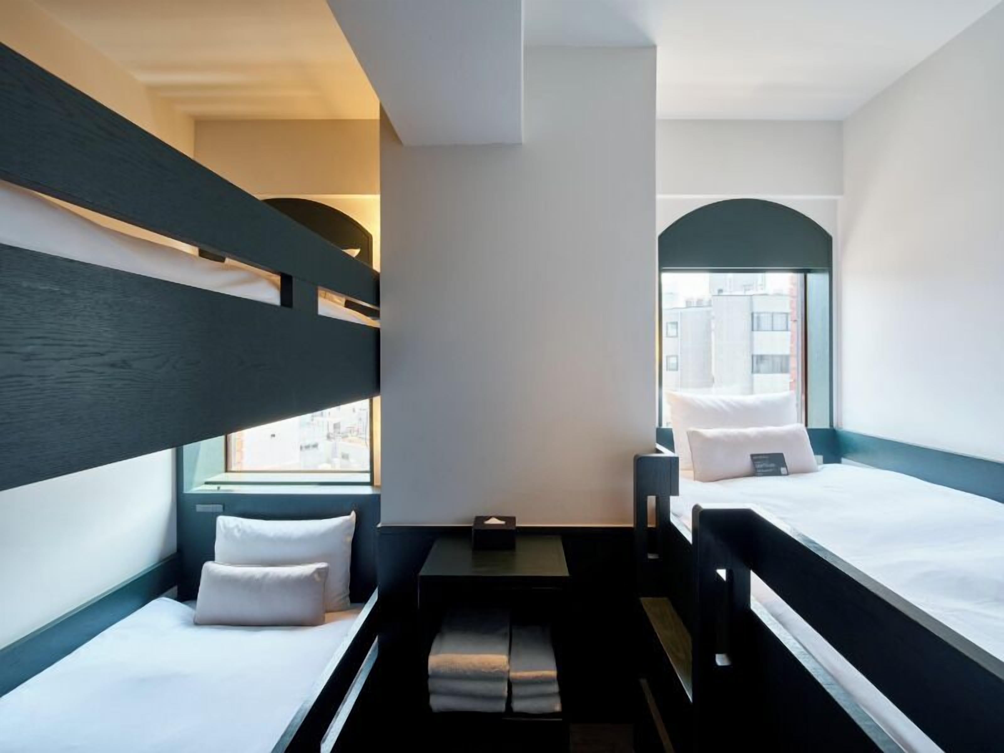 A hotel room with bunk beds, a small table, and a window with a view of buildings.