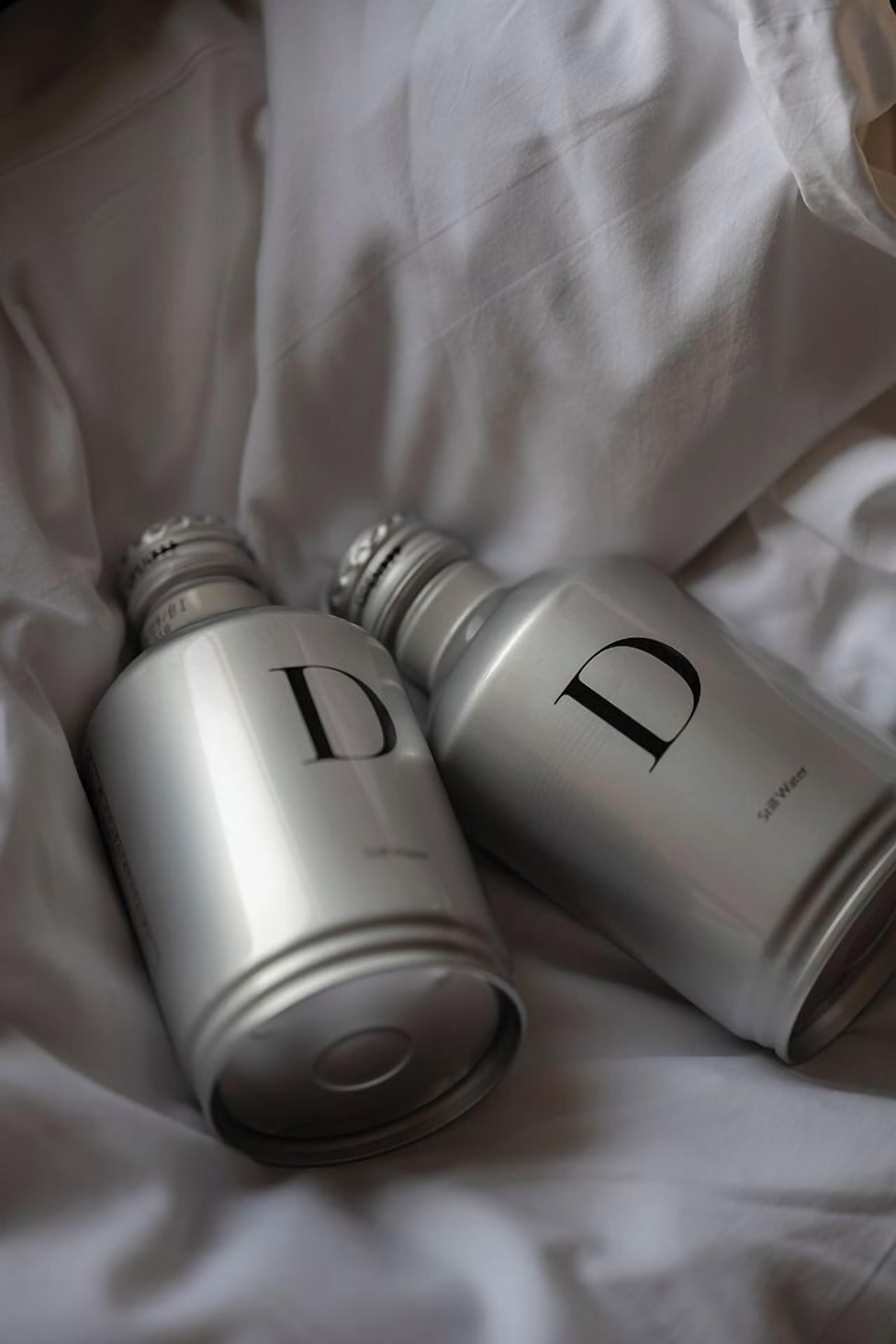 Two metallic bottles with a prominent letter 'D' on a white fabric surface.