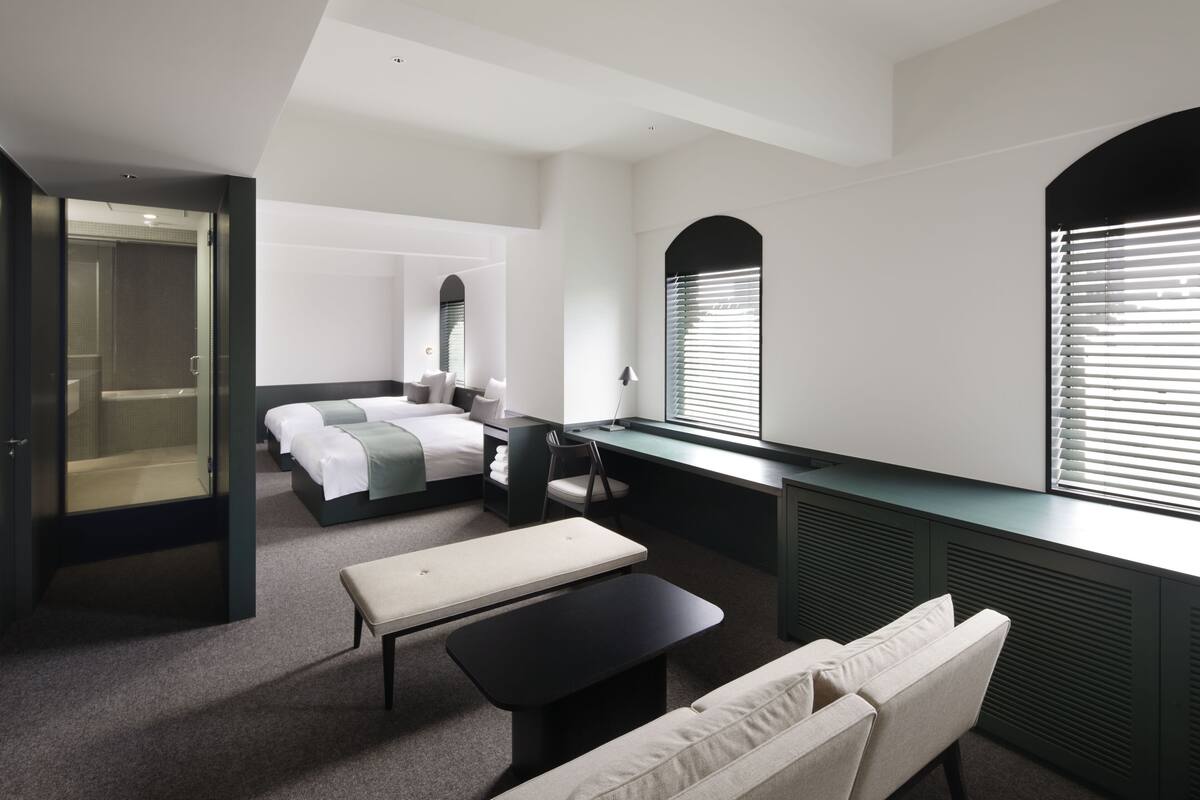 A modern hotel room with a bed, a desk, a bench, and a sofa.